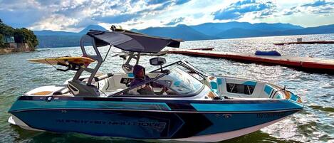A boat with a canopy, labeled 'SUPER AIR NAUTIQUE,' on calm water with mountains in the background.