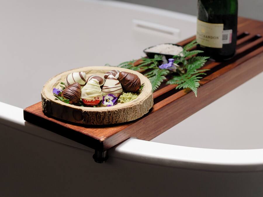 Una bandeja de madera con bombones y una botella de champán sobre una mesa blanca.