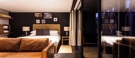 A modern hotel room with a large bed, a leather sofa, and a glass partition.