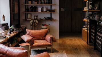 Una habitación acogedora con un sillón de cuero, estantes de madera con diversos objetos y una pequeña mesa redonda.
