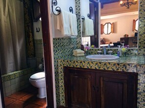 A bathroom with a toilet, a sink with a mirror, and patterned tiles. - Casita Santa Rosa (Antigua Guatemala)