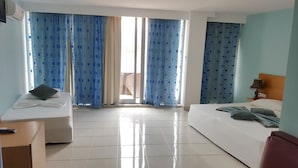 A hotel room with two beds, a small table, and a window with blue curtains. - Hotel Cachoeira Tarrafal (Tarrafal)