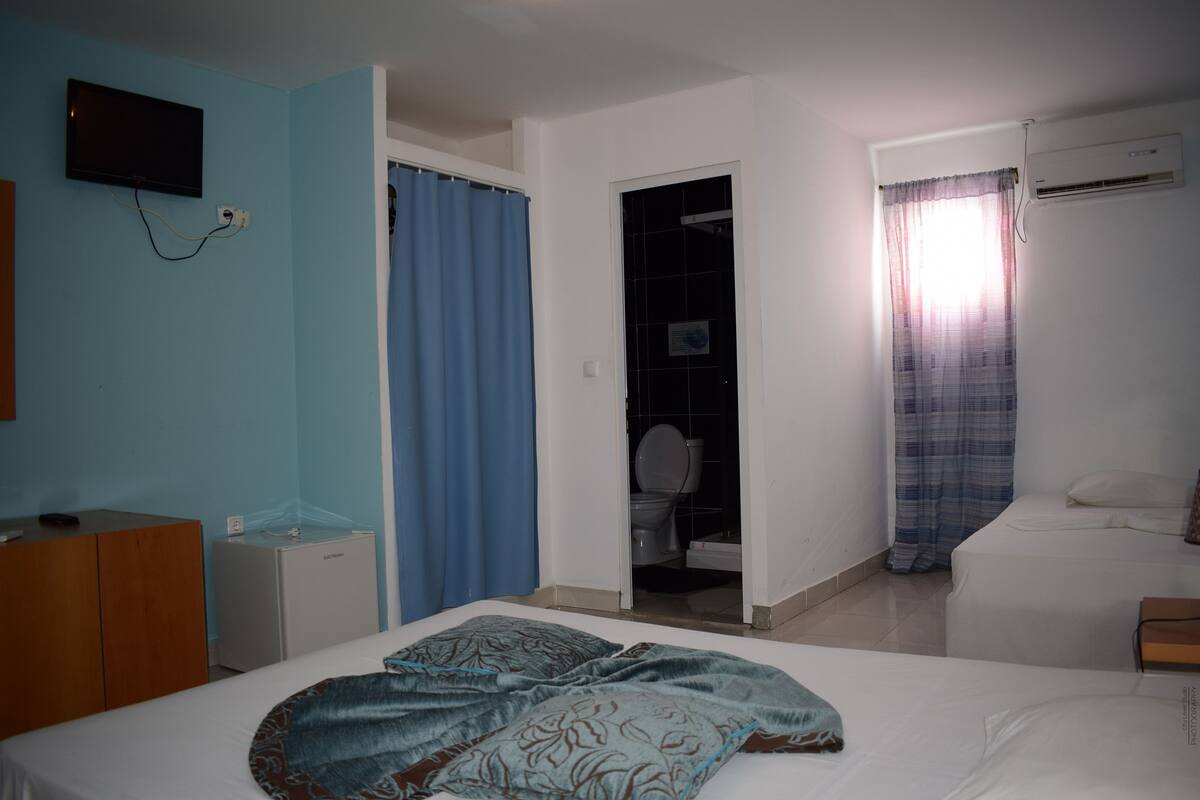 A bedroom with a bed, a TV mounted on the wall, a small desk, and a bathroom visible through an open door.