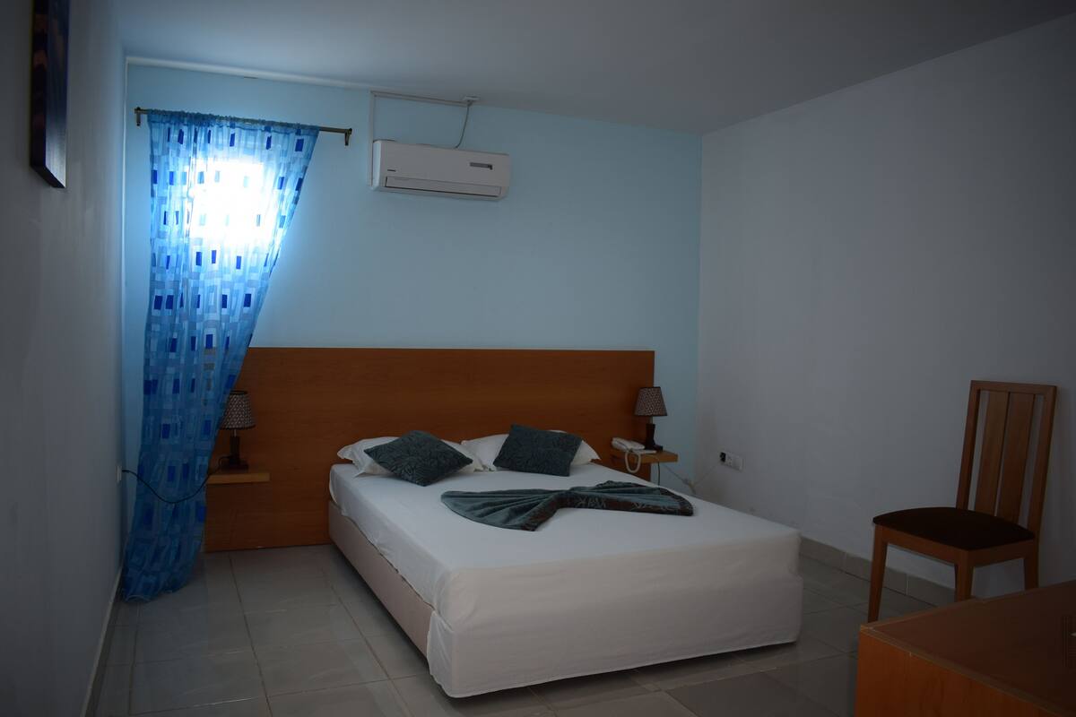 A bedroom with a bed, a chair, a nightstand, and an air conditioning unit.