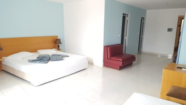 Una habitación de hotel con una cama, una silla roja, un escritorio de madera y una mesa blanca.