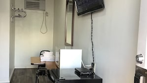 Habitación de hotel moderna con televisor de pantalla plana montado en la pared, un escritorio con una computadora portátil, una silla y una mesita con toallas.