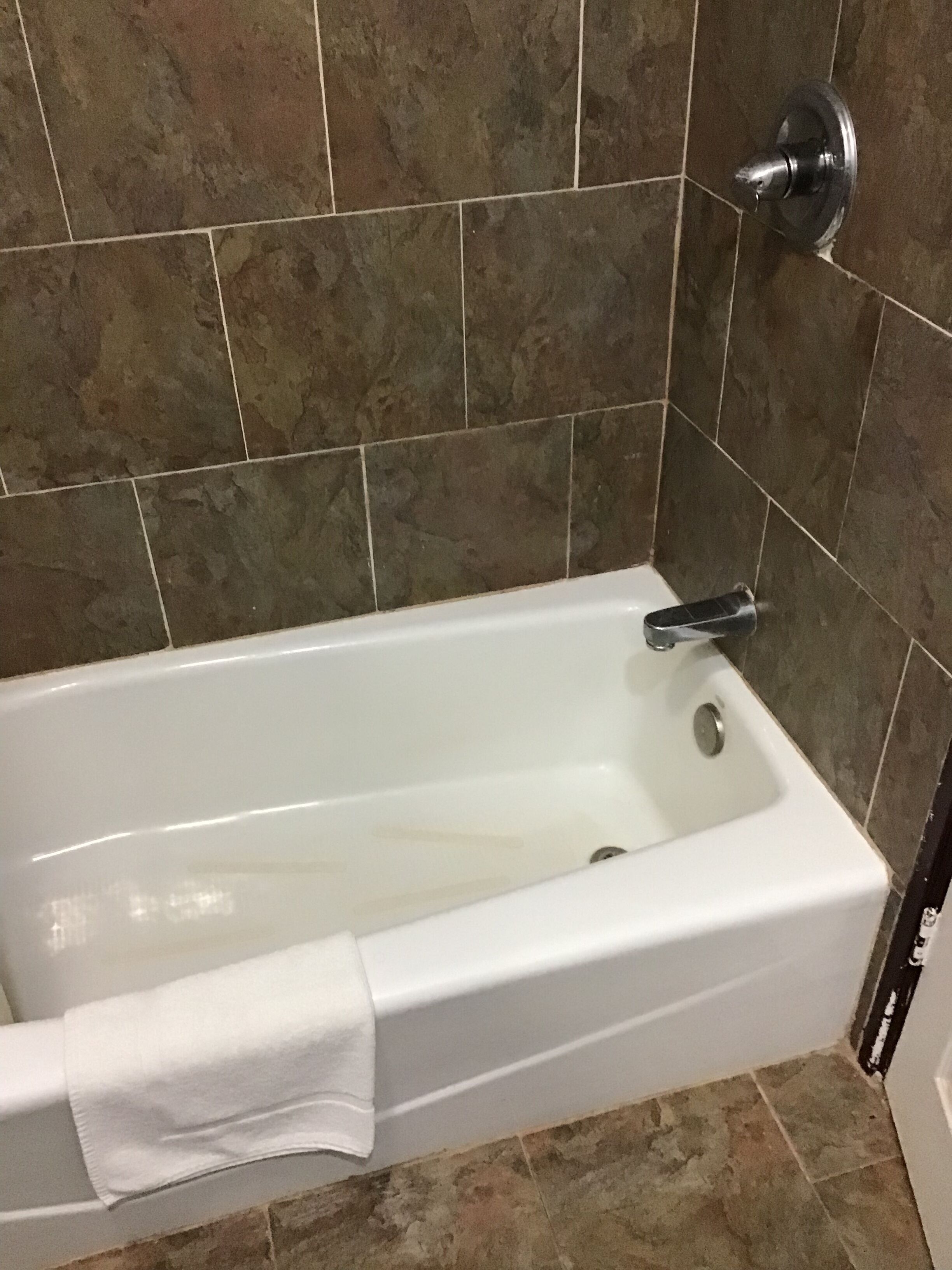 Una bañera blanca con un cabezal de ducha manual, frente a un fondo de baldosas de piedra marrón.