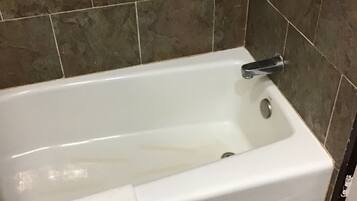 Una bañera blanca con un cabezal de ducha manual, frente a un fondo de baldosas de piedra marrón.