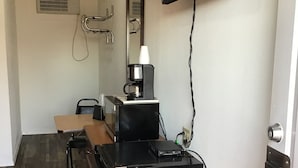 Una kitchenette compacta con cafetera, un refrigerador pequeño y un televisor de pantalla plana montado en la pared.