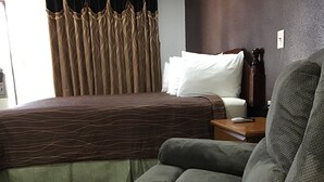 Una habitación de hotel con una cama, una silla, una mesita de noche y un enchufe.