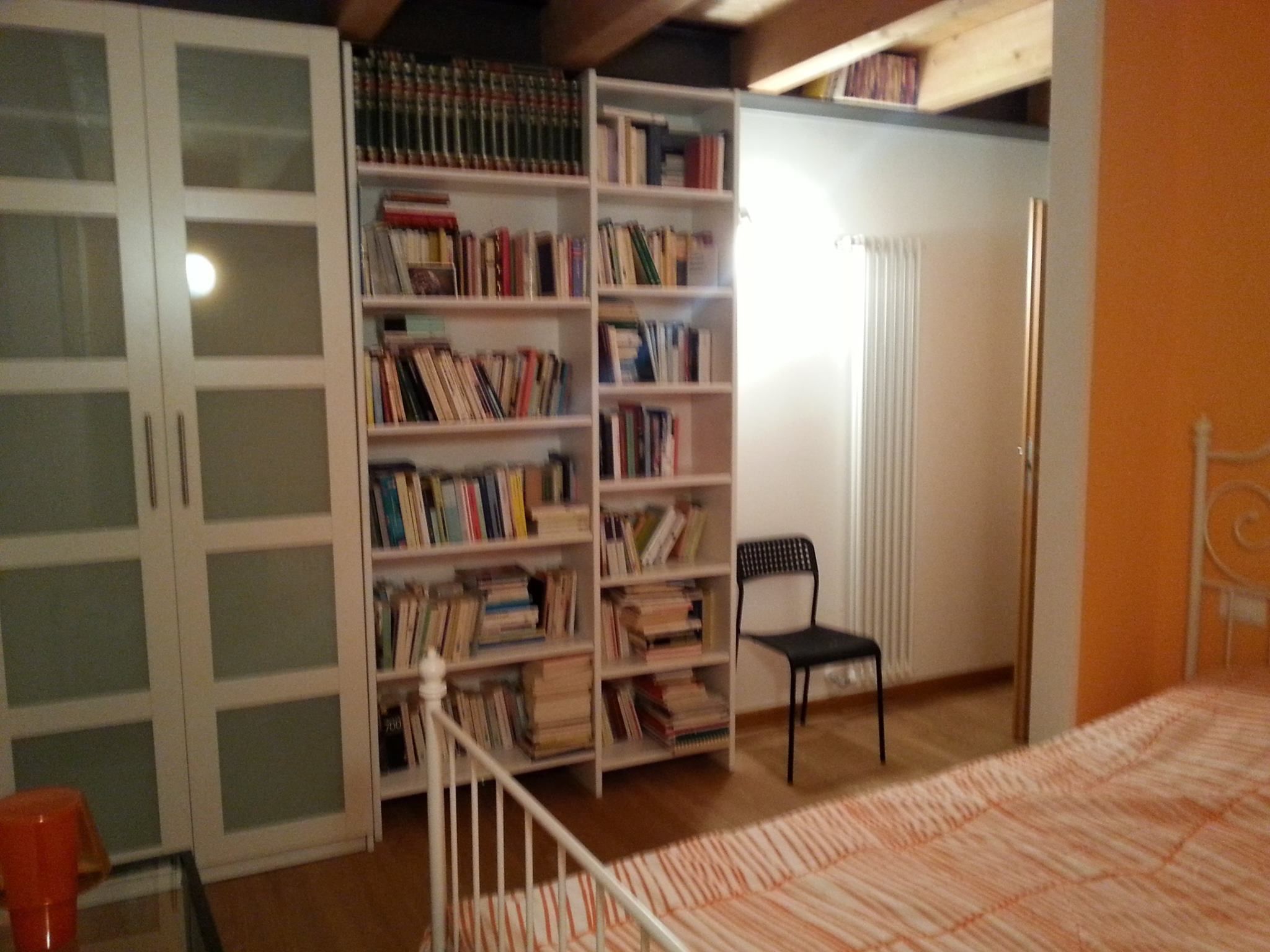 A bedroom with a bed, a bookshelf, a chair, and a wardrobe.