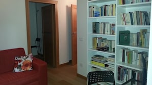 A room with a red sofa, a bookshelf filled with books, a wooden door, and a black chair. - B&B Al Gatto Nero (Borgo Valsugana)