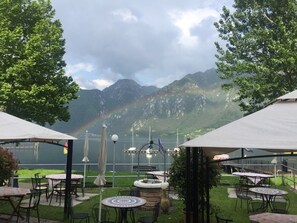 An outdoor seating area with tables and umbrellas overlooking a lake and mountains. - Hotel al Lago (Anfo)