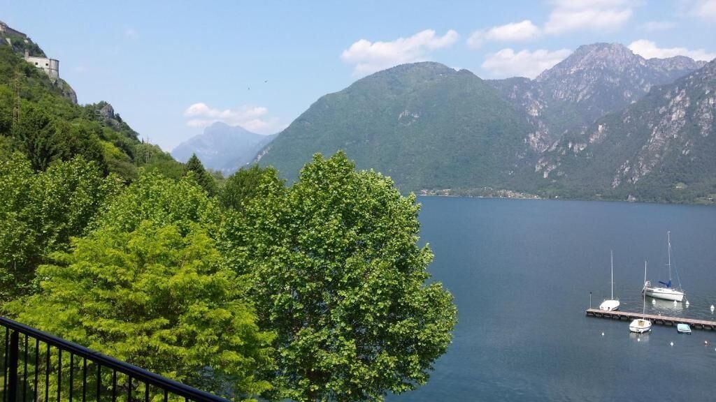 Un lago con barche, un molo e montagne sullo sfondo.
