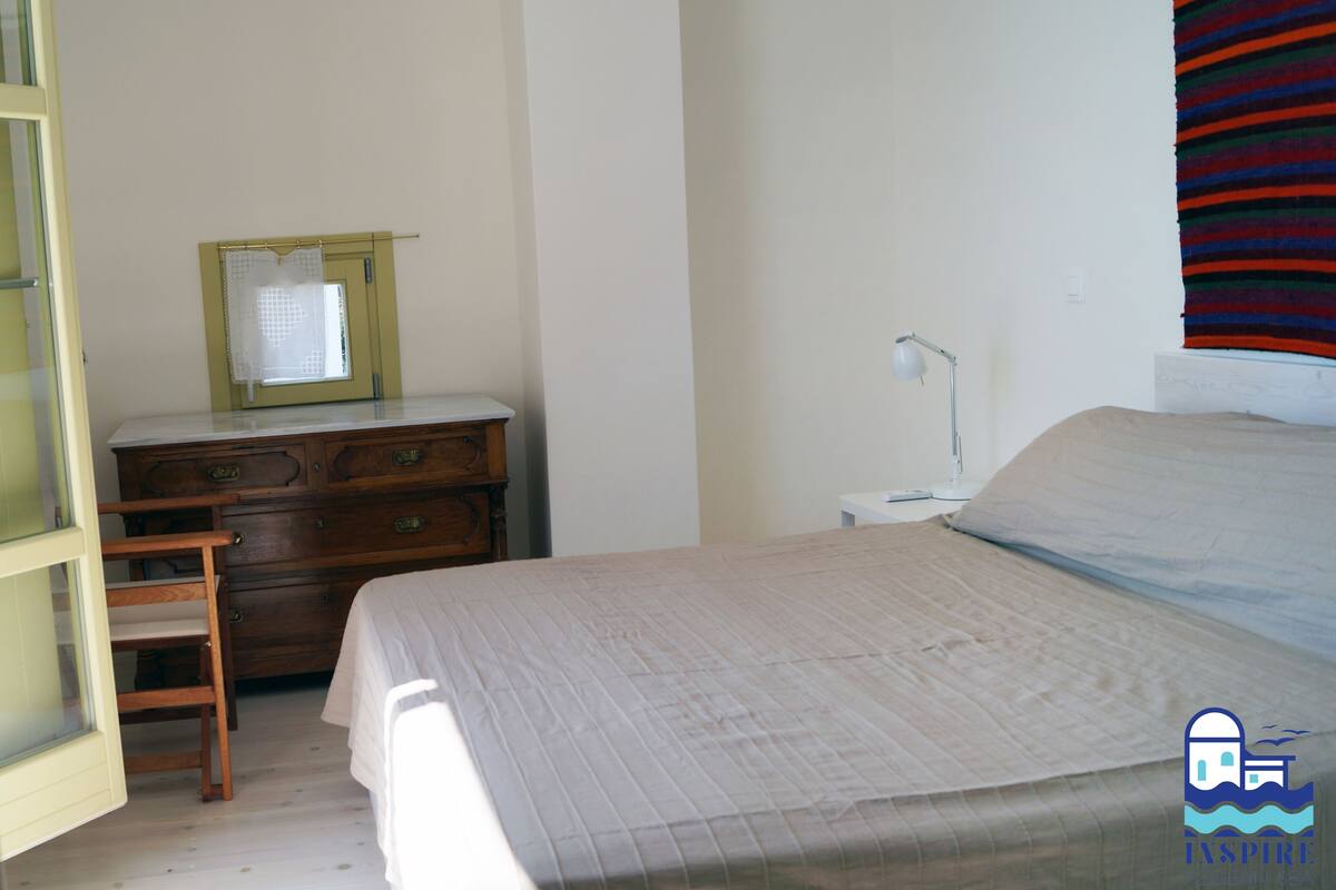 Ein Schlafzimmer mit einem Bett, einer Holzkommode, einem Schreibtisch mit Lampe und einem Fenster mit Vorhang.
