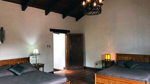 A room with two wooden beds, a chandelier, a door, and a lamp. - Casita San Sebastián (Antigua Guatemala)