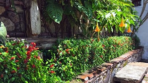 A stone wall with a brick pathway, lush greenery, and hanging orange flowers. - Casita San Sebastián (Antigua Guatemala)
