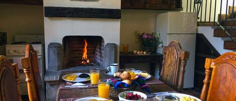 Una mesa de comedor dispuesta con cosas para el desayuno, una chimenea, armarios de madera y una escalera.