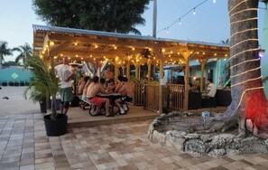 An outdoor seating area with tables and chairs under a wooden pergola with string lights. - Hoosville Hostel (Florida City)