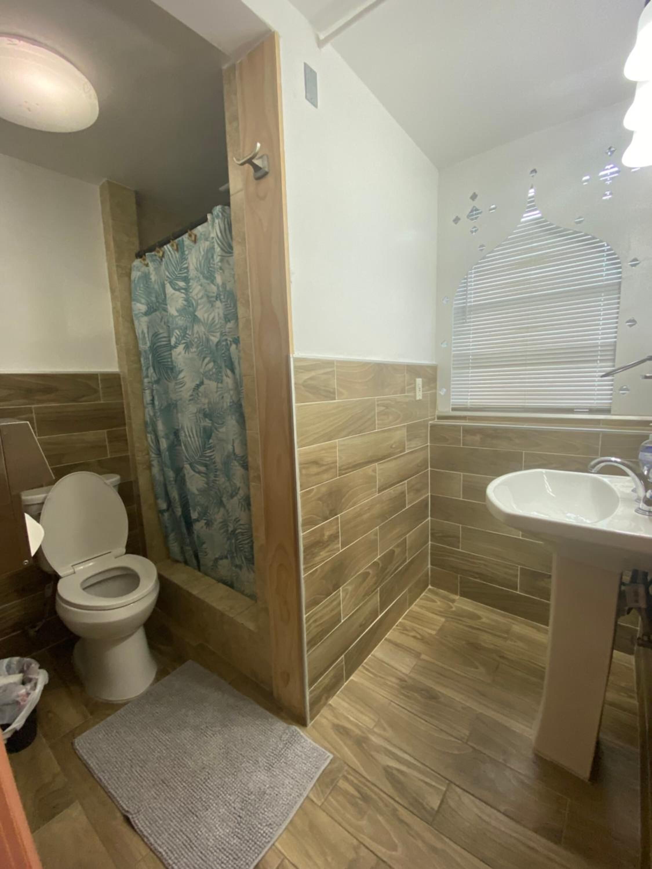 Un bagno con toilette, doccia, lavandino e pavimento in legno.
