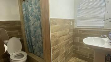 Un bagno con toilette, doccia, lavandino e pavimento in legno.