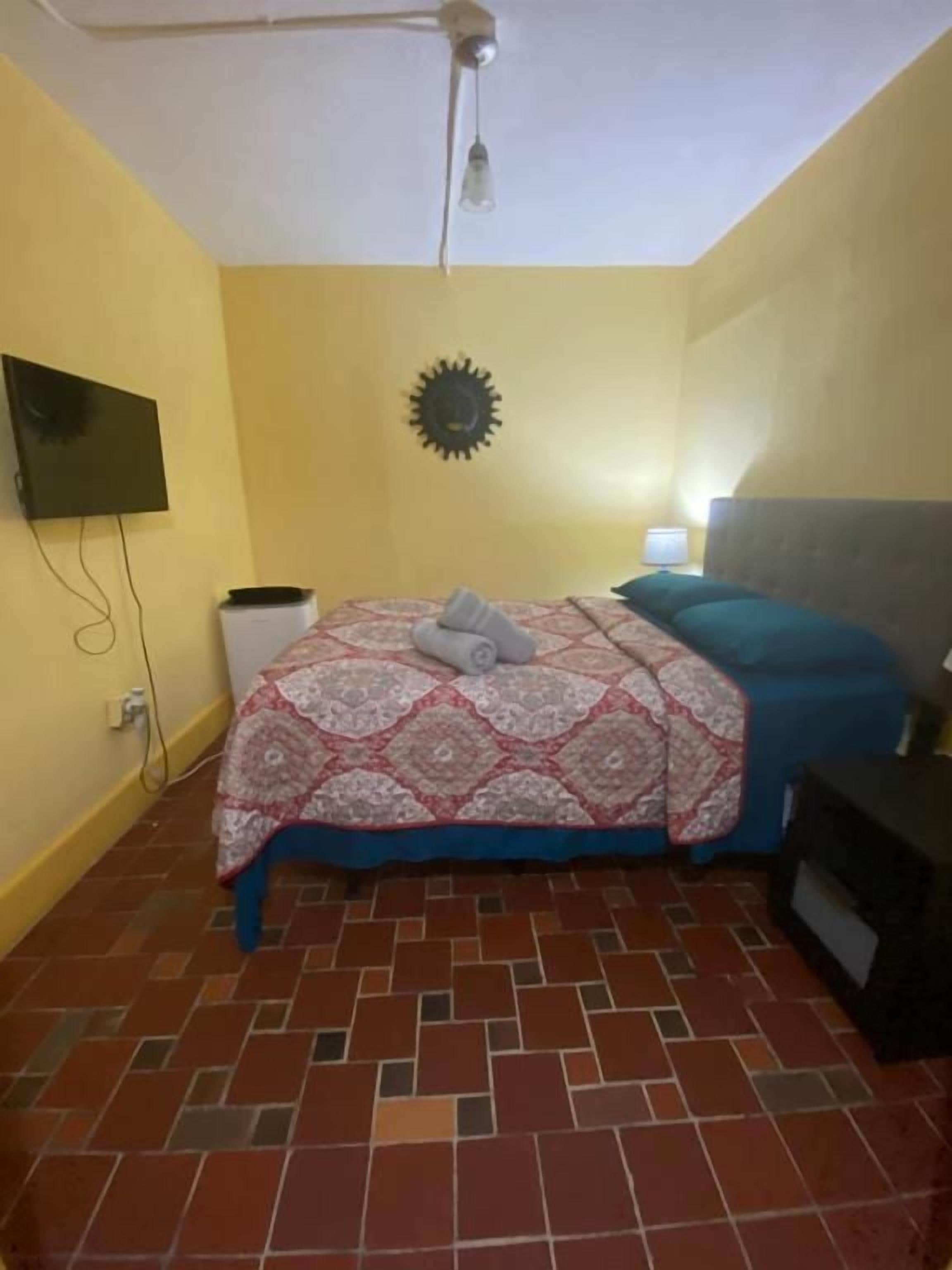 A bedroom with a bed, a television, a wall-mounted light, and a ceiling fan.