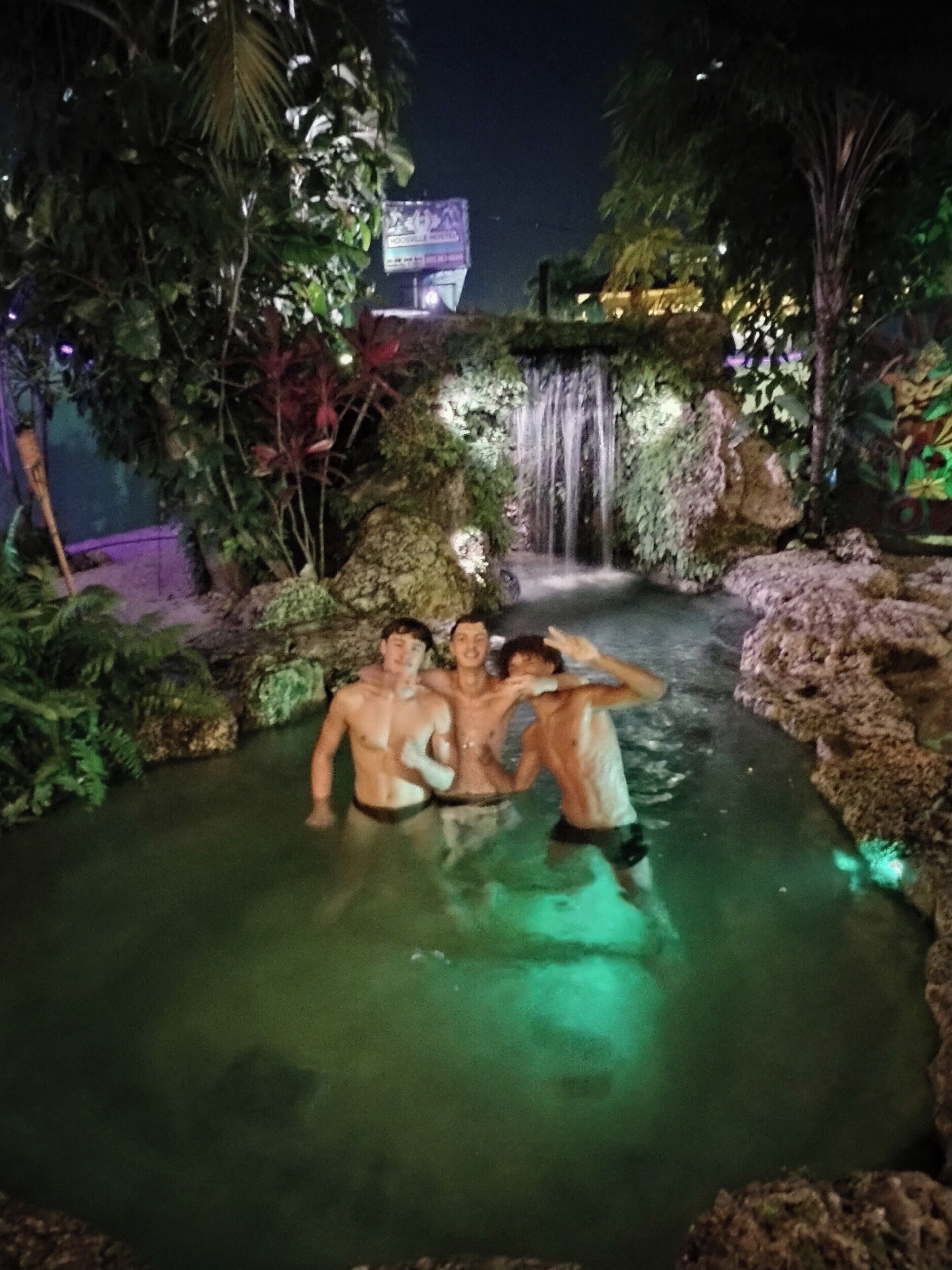 Ein Poolbereich im Freien bei Nacht mit einem Wasserfall und üppiger Vegetation.