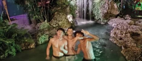 Ein Poolbereich im Freien bei Nacht mit einem Wasserfall und üppiger Vegetation.