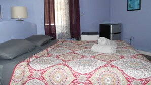 A bedroom with a large bed, a bedside table, a lamp, a heater, and a window with curtains. - Hoosville Hostel (Florida City)