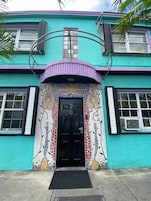 Um edifício com entrada em mosaico colorido, uma porta preta com o número 20 e dois aparelhos de ar condicionado nas janelas.