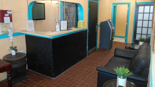 A reception area with a black reception desk, a blue-framed mirror, a black couch, and a small table with a plant. - Hoosville Hostel (Florida City)