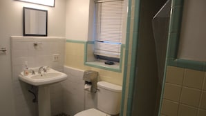 A small bathroom with a pedestal sink, toilet, and a window with blinds. - Hoosville Hostel (Florida City)