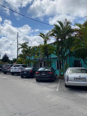 Un parking avec plusieurs voitures, un bâtiment turquoise et des palmiers.