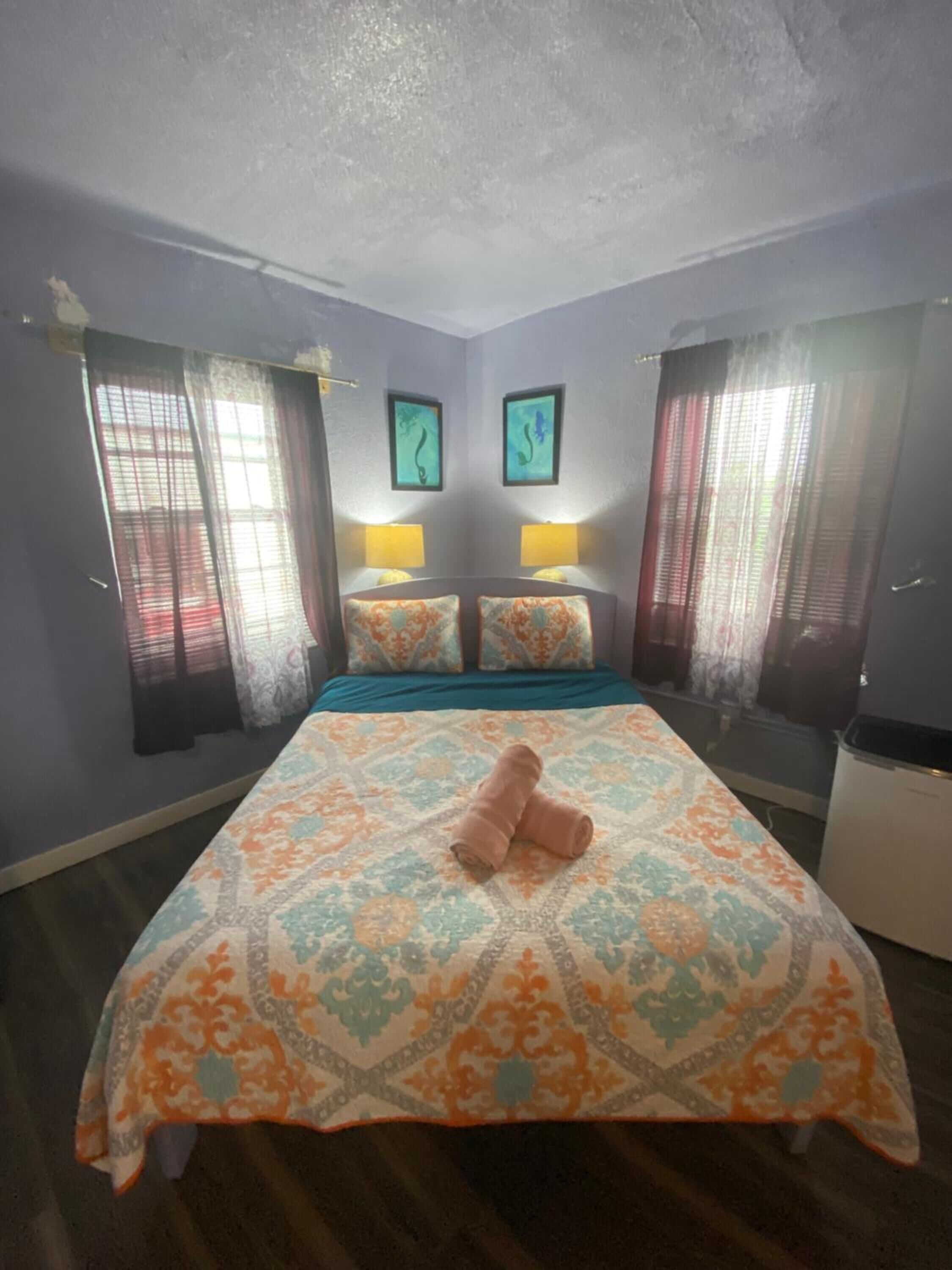 Una camera d'albergo con un letto, due lampade sui comodini, una finestra con tende e una parete decorata con due opere d'arte incorniciate.