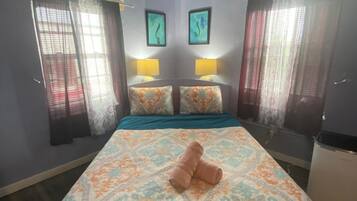 Una camera d'albergo con un letto, due lampade sui comodini, una finestra con tende e una parete decorata con due opere d'arte incorniciate.