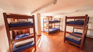 Una habitación con literas ubicadas en un rincón, suelo de madera y una lámpara en el techo.
