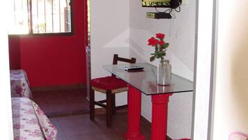 Una habitación pequeña con una mesa de comedor, un televisor en la pared y una ventana con rejas.