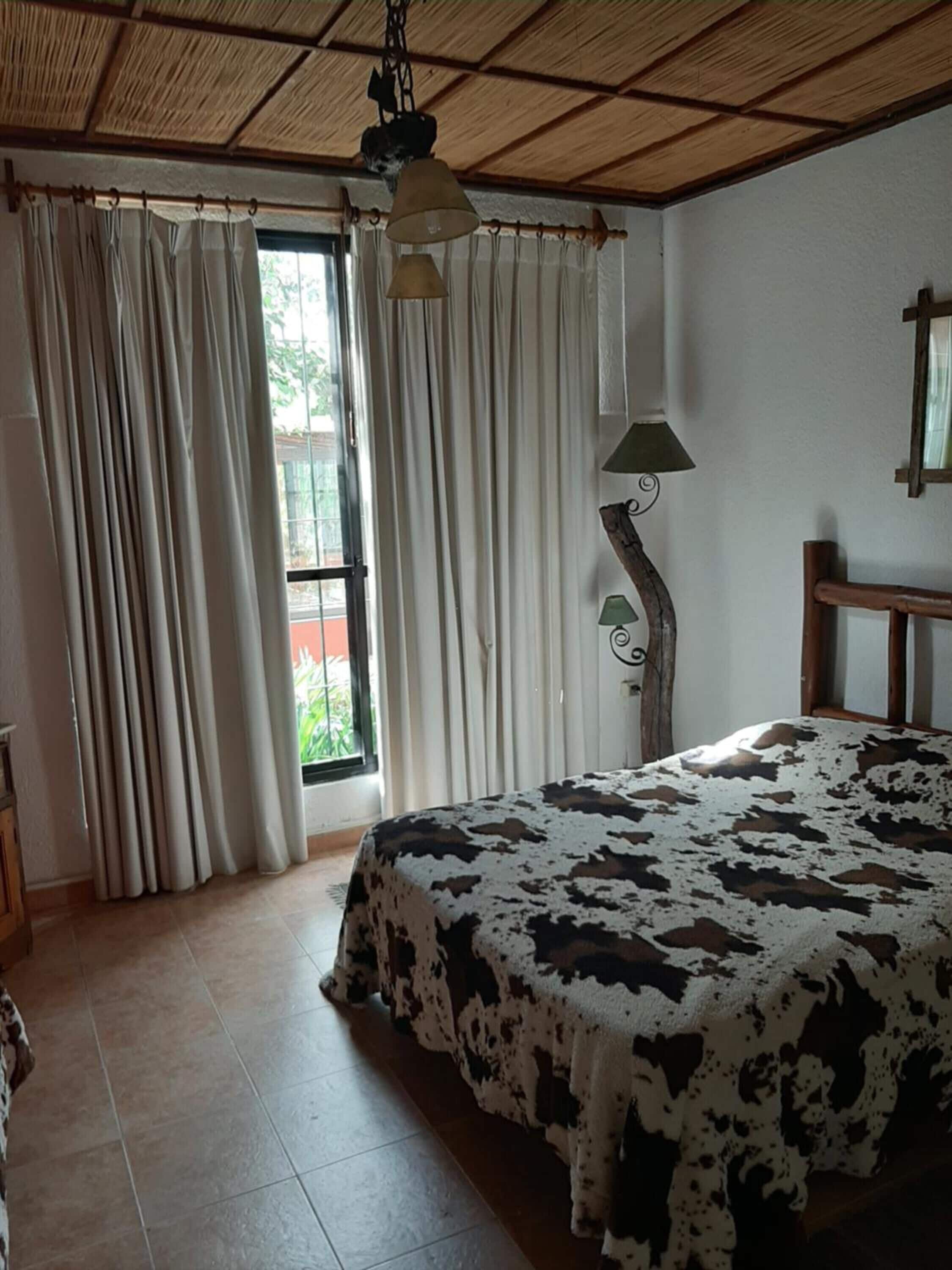 A bedroom with a bed, curtains, a lamp, and a window.