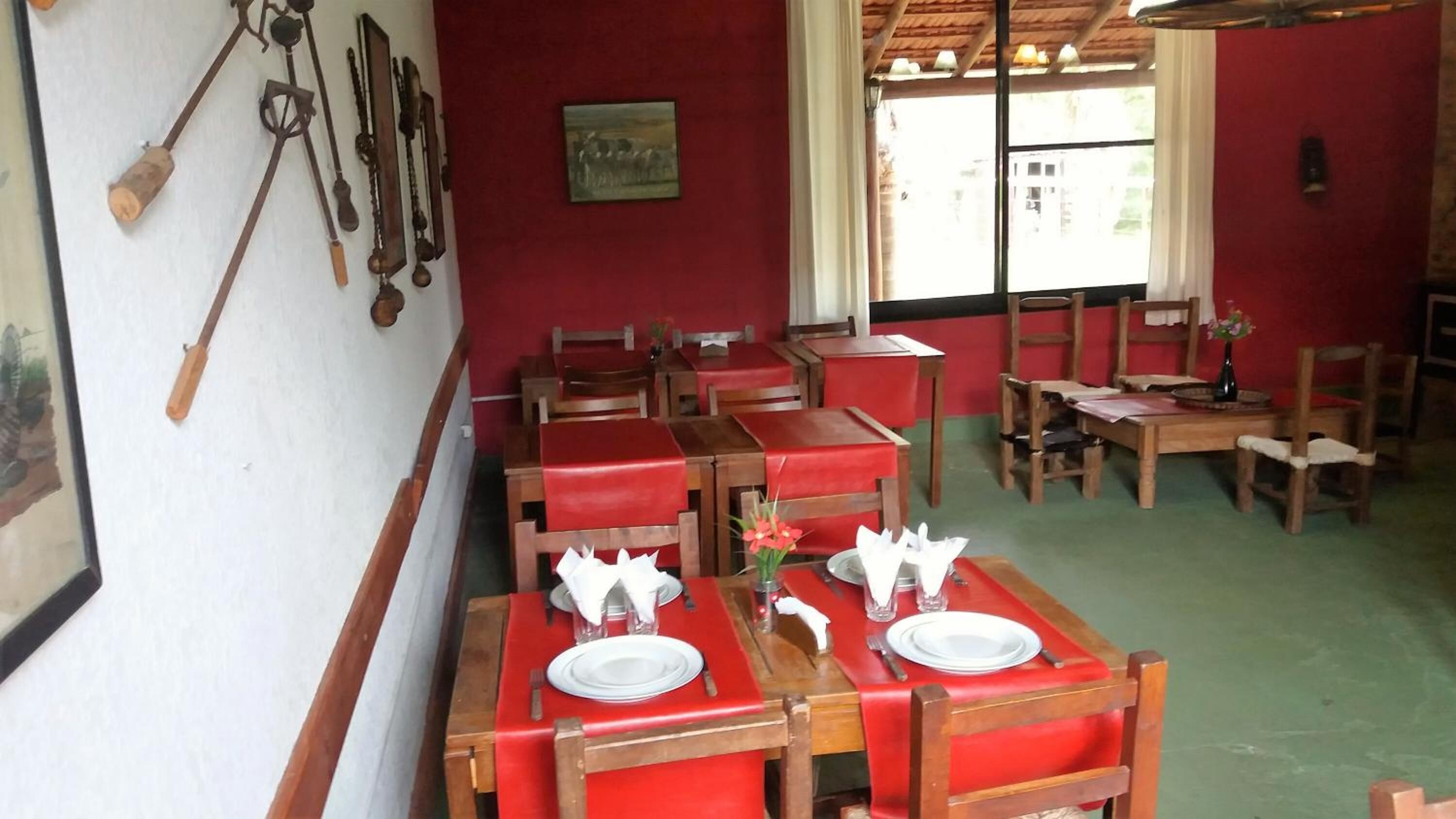 A restaurant with red booths and wooden tables, some with white napkins and plates.