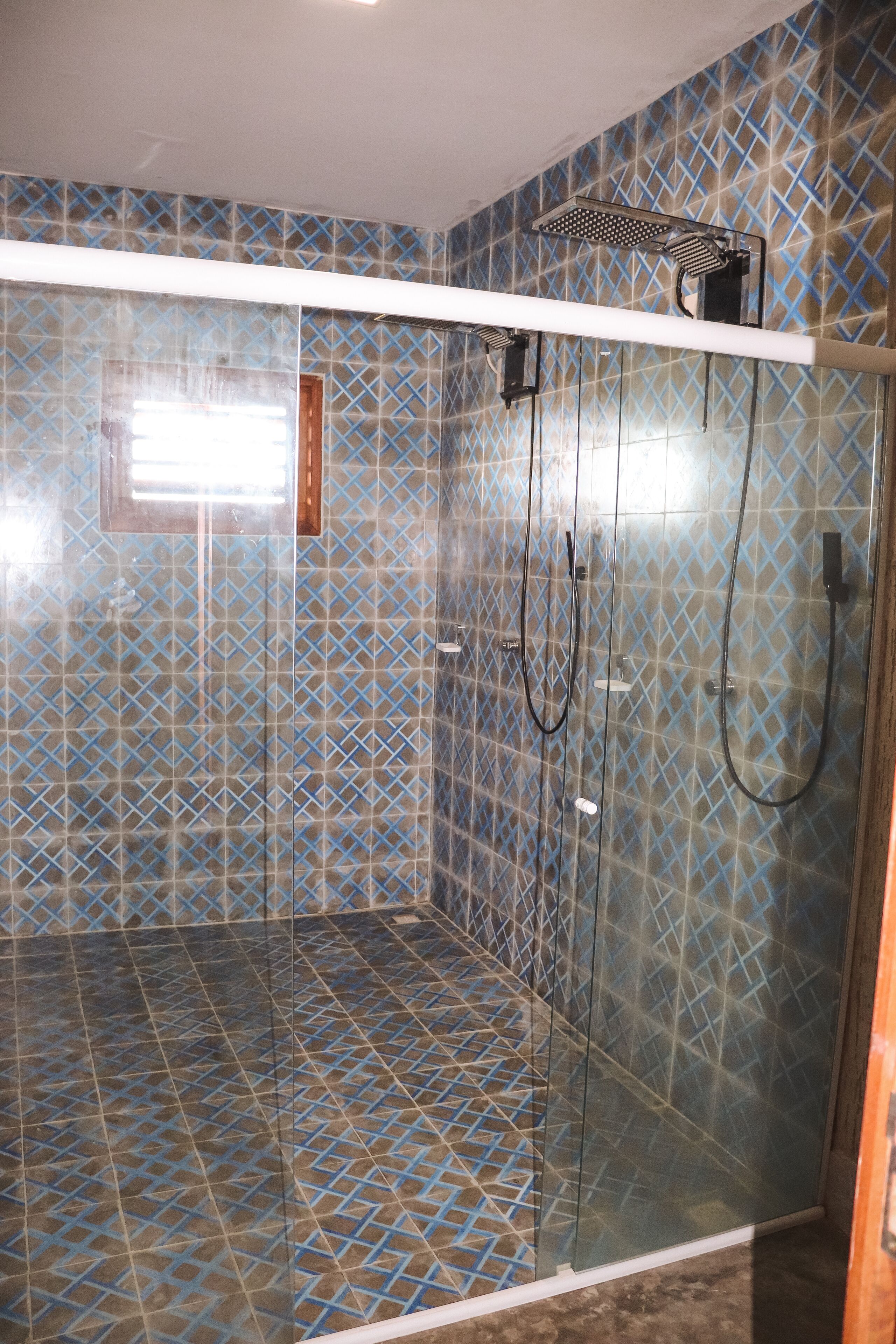 A shower with a glass door and a patterned tile wall.