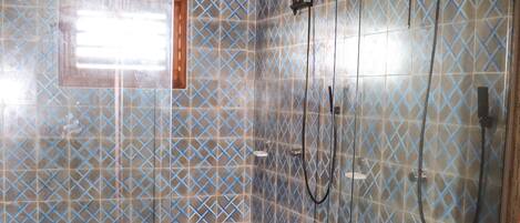 A shower with a glass door and a patterned tile wall.