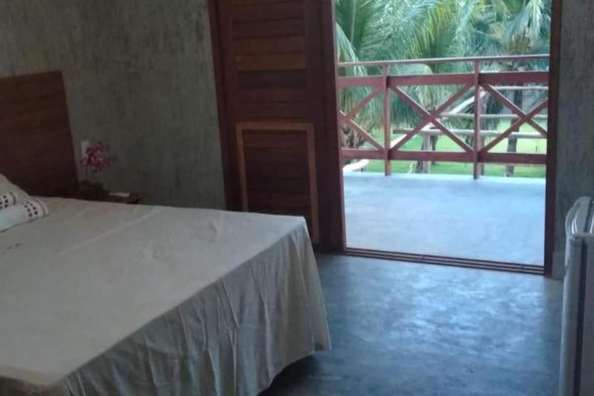 A bedroom with a bed, a nightstand, a small table, and a door leading to an outdoor area with a red railing.