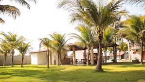 Un patio con palmeras, un edificio de techo de paja y un césped.