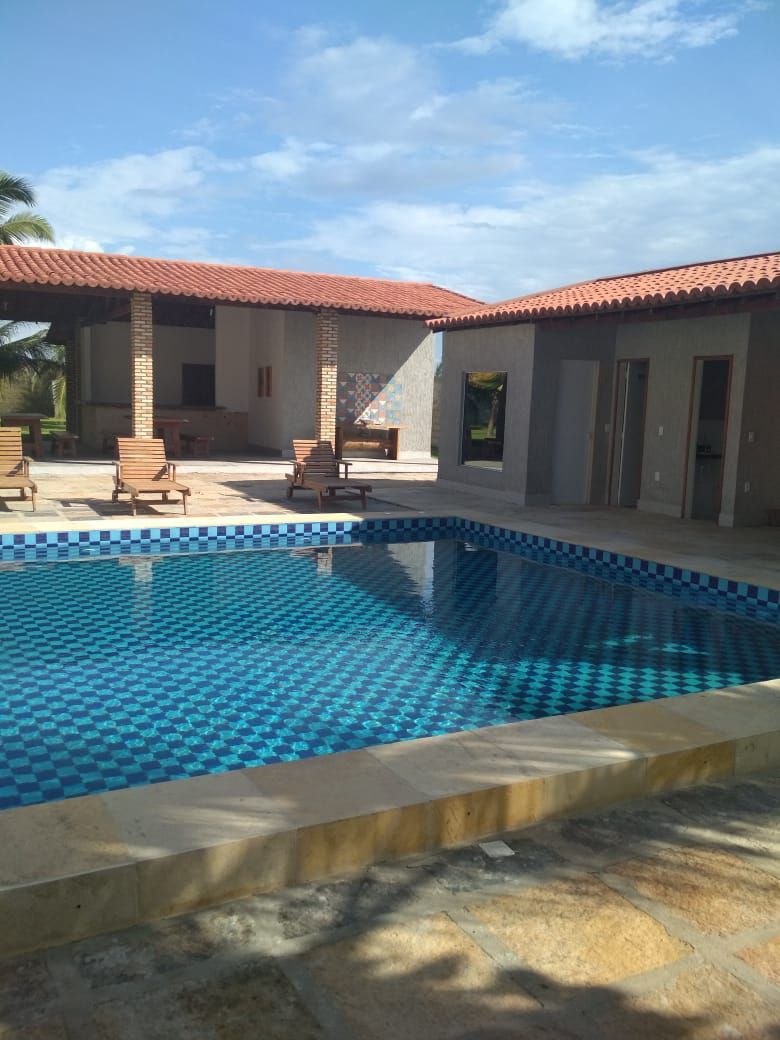 A swimming pool with a tiled edge, surrounded by lounge chairs and a covered patio area.