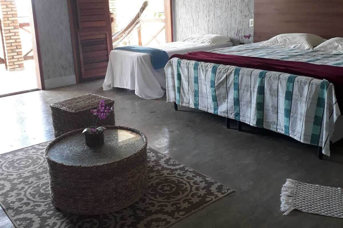 A bedroom with a bed, a woven coffee table, a patterned rug, and a wooden door.