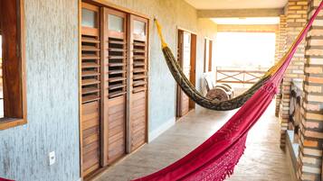 A hammock strung between wooden shutters in a corridor with a brick wall and a view of the outside.