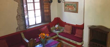 A cozy living room with a red sofa, a wooden table with a vase of flowers, and a fireplace.