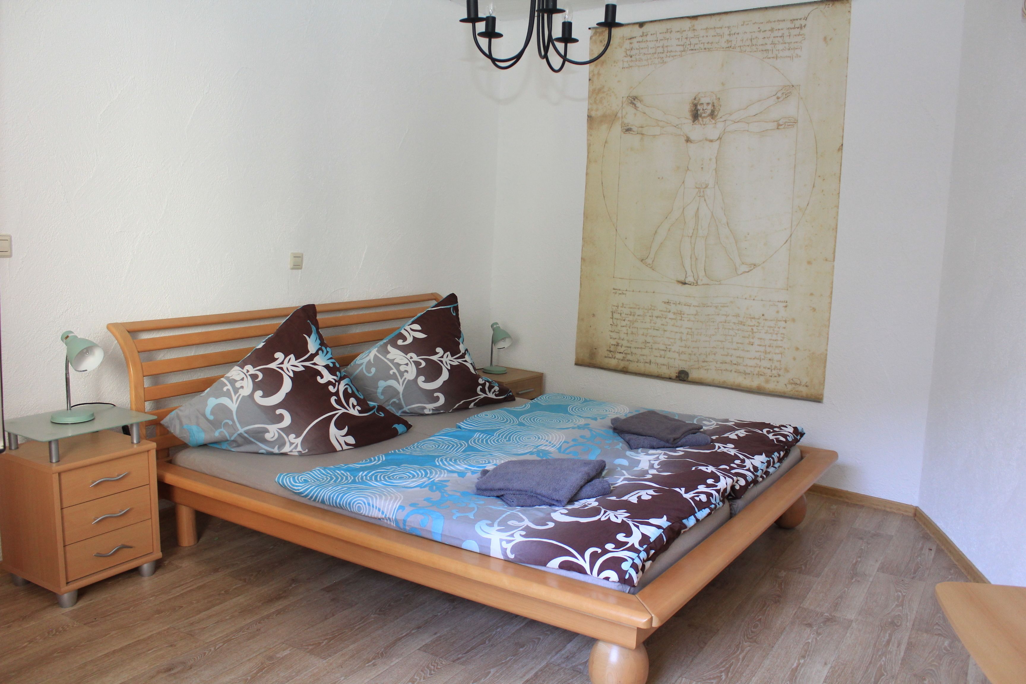 A bedroom with a wooden bed, patterned bedding, a nightstand with a lamp, and a large framed artwork on the wall.