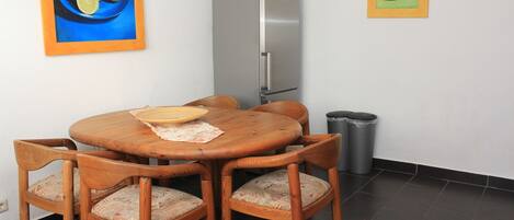 Un comedor con una mesa y sillas de madera, un refrigerador y un cubo de basura.