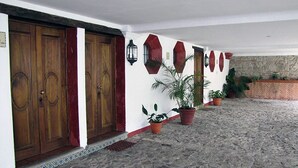 A building with a stone floor, wooden doors, and potted plants. - Casita San Francisco (Antigua Guatemala)